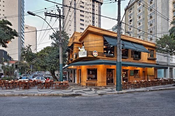 Cervejas no balde e comida de boteco, em ambiente rústico, descontraído e animado, com mesinhas na calçada.